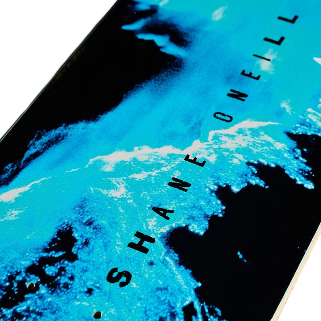 A close-up of AApril Shane Blue Flow skateboard deck featuring a graphic print of a blue and black ocean wave with the text 'SHANE O'Neill' printed diagonally in black.