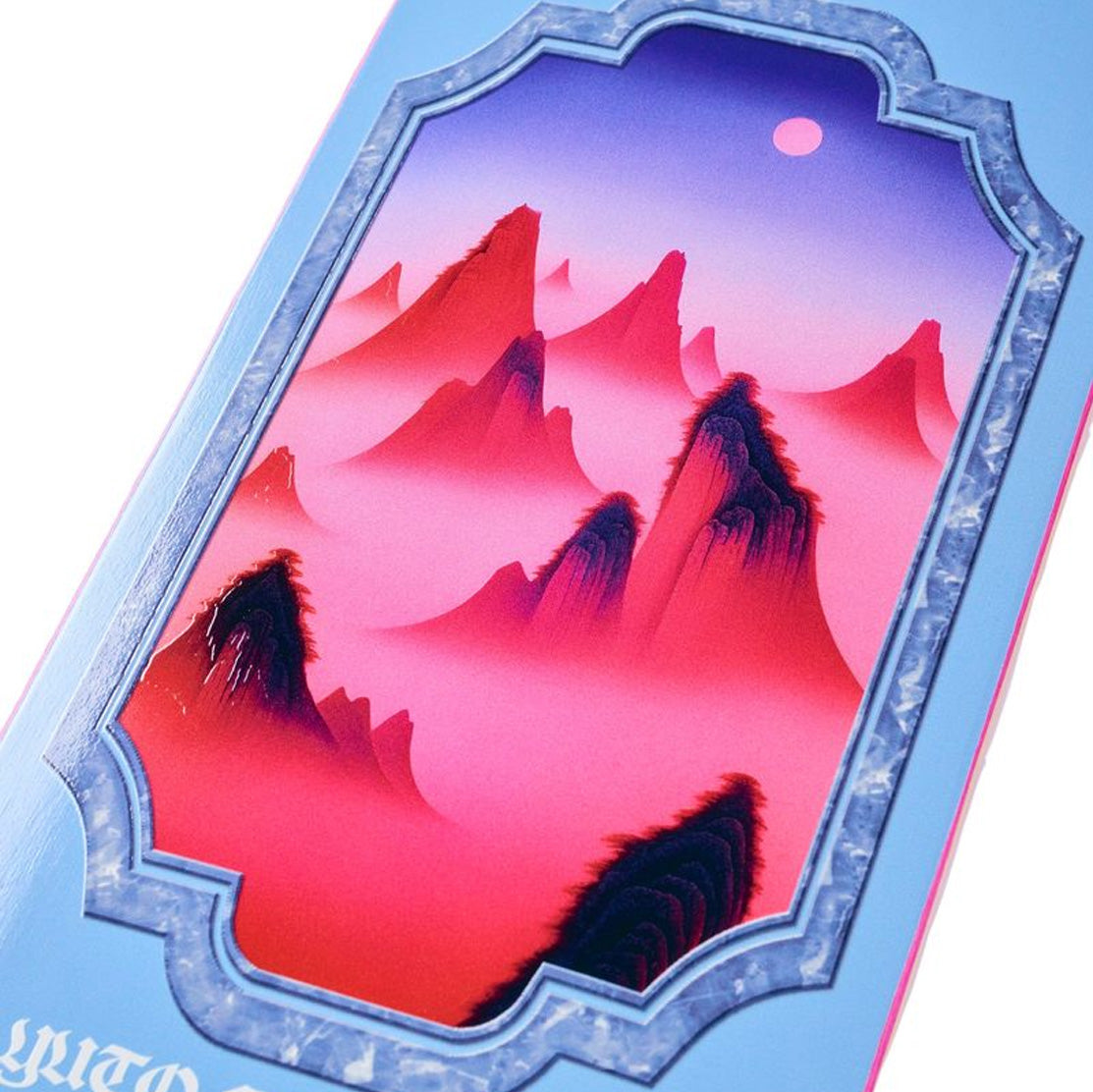 A close-up of the Yuto Misty April deck decoratiwith a stylized mountain landscape with layered pink, red, and purple peaks inside an ornate blue border.